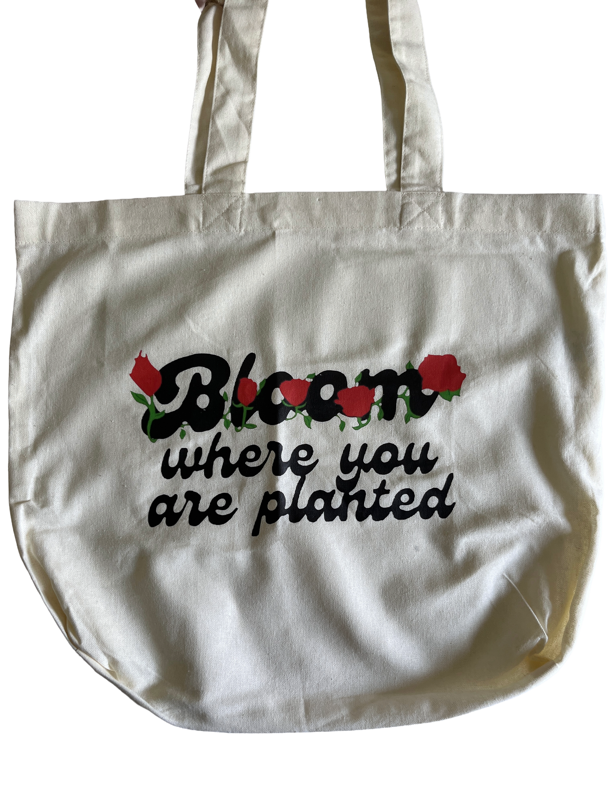 White tote bag with floral design and text that says bloom where you are planted on a white background