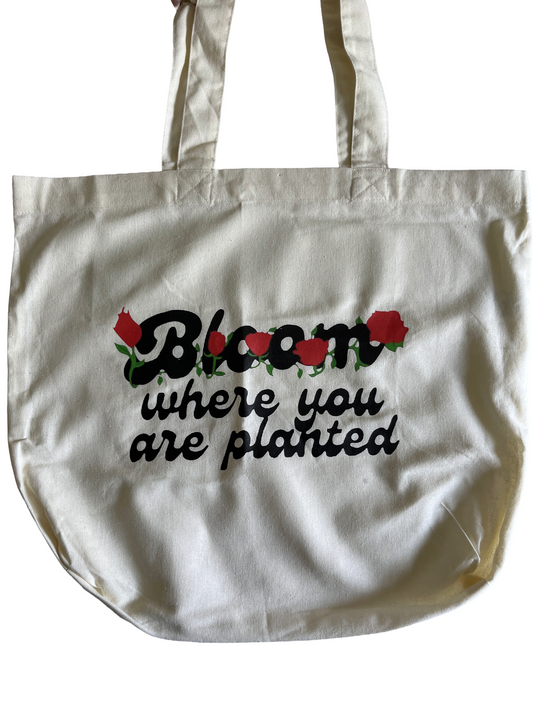 White tote bag with floral design and text that says bloom where you are planted on a white background